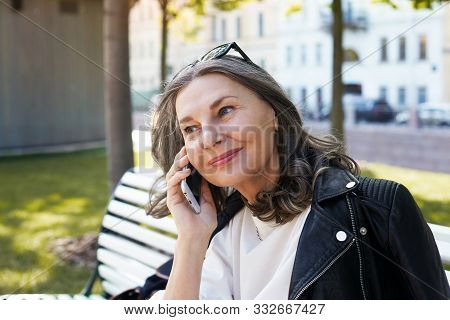 Cheerful Beautiful European Female In Her Fifty Enjoying The Nice Summer Weather Outdoors, Sitting O
