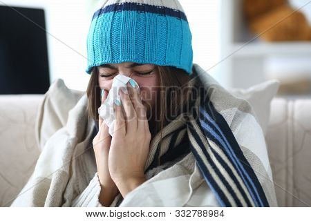 Portrait Of Beautiful Woman Blowing Into White Tissue And Closing Cute Eyes. Poor Girl Sitting Indoo