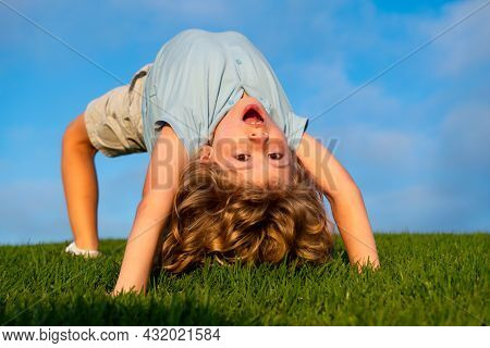 Happy Boy Doing A Headstand On The Grass In The Summer Sunshine. Funny Happy Little Child Standing O