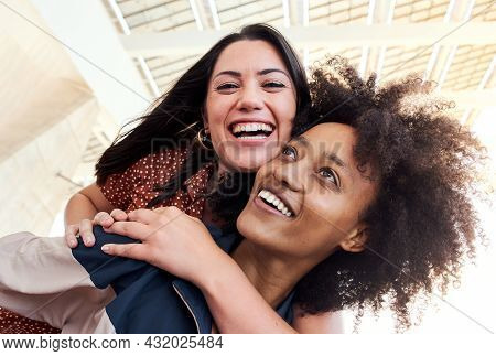 Young Lesbian Couple In Love Smiling Looking At The Camera. The Girl Is Riding A Piggyback To Her Fr