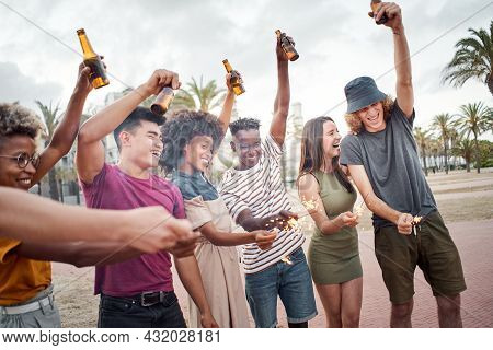 Group Of Friends Celebrating With Sparkles And Beers. People Of Different Races Having A Good Time A