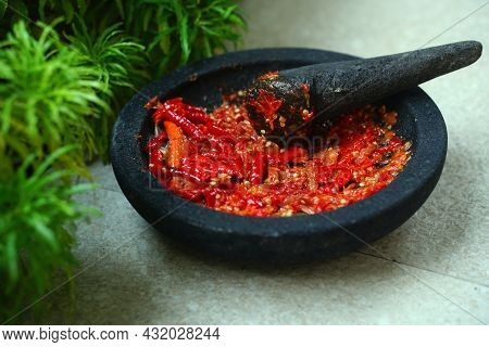 Red Chili Sauce On A Stone Mortar And Pestle. There Is Greenery Beside