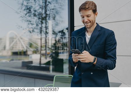 Pleased Handsome Male Ceo Or Director Holds Mobile Phone Waits For Call Scrolls Social Networks Whil