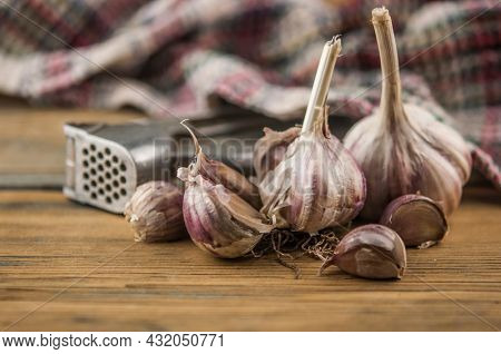 Organic garlic with metal press. Fresh garlic cloves and garlic bulb on a wooden table. Garlic for healthy eating. Concept of spices for healthy cooking. Closeup