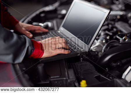 Crop Male Using Netbook With Black Screen While Checking Motor Of Modern Vehicle During Work In Gara