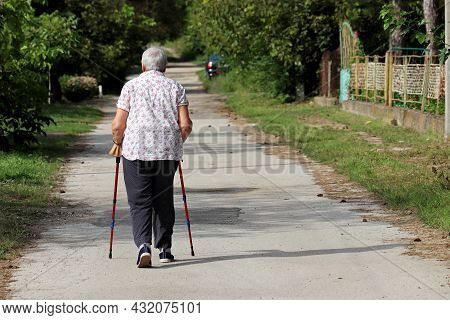 Old Woman Walking With A Cane On A Street. Limping Person, Diseases Of The Spine, Life Of Elderly Pe