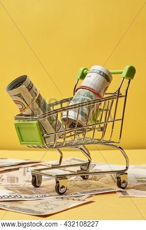 Buying Us Dollars In Uzbekistan. Us Dollars Roll In Shopping Trolley And Pile Of Uzbek Sums. Uzbek M
