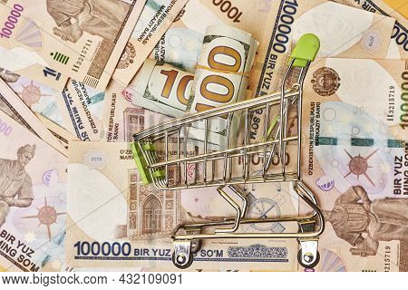 Buying Us Dollars In Uzbekistan. Us Dollars Roll In Shopping Trolley And Pile Of Uzbek Sums. Uzbek M