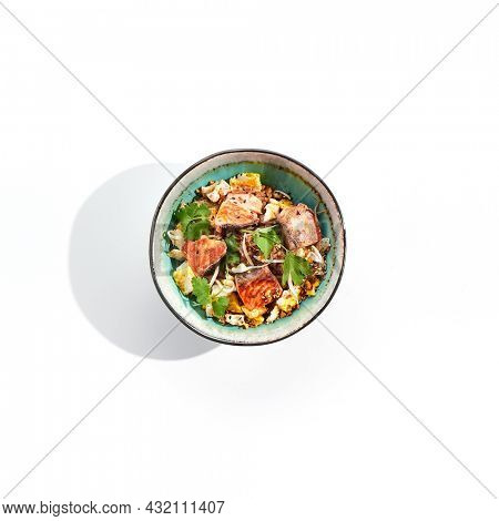 Asian traditional dish - fried rice with egg, vegetables, and salmon. Pan asian wok with rice, egg and fish on white background. Nasi goreng with salmon on isolated background with shadows