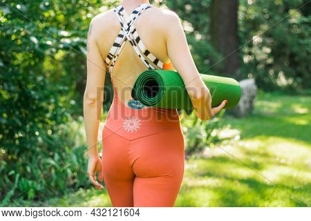 Kyiv, Ukraine 08.08.2021: Woman In Orange Yoga Jumpsuit With Her Back Turned Holding A Twisted Yogam