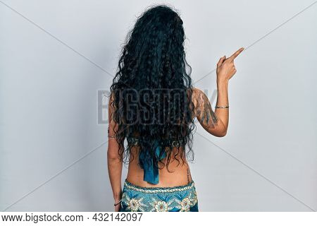 Young woman wearing bindi and traditional belly dance clothes posing backwards pointing ahead with finger hand 