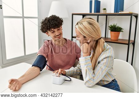 Young couple smiling happy measuring blood pressure using tensiometer at home.