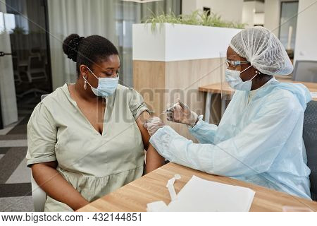 Serious African-american Woman In Medical Mask Looking At Doctor Giving Her Dose Of Vaccine Against 