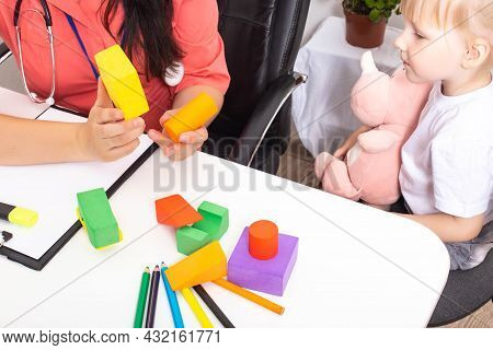 The Doctor Shows The Multi-colored Figures Of The Constructor To A Little Girl 3-4 Years Old. Develo