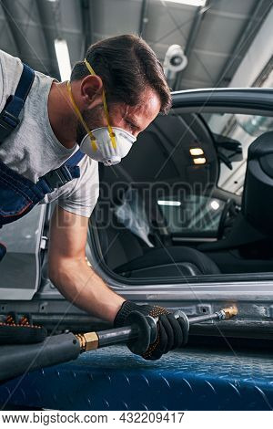 Tense Man Using Sliding Hammer For Straightening Car Surface