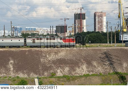 An Electric Locomotive On The Railroad Tracks Against The Backdrop Of A City Under Construction.