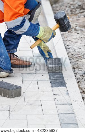 A Worker In Blue And Orange Overalls Bangs The Paving Slabs With A Rubber Mallet. Vertical Image, Se