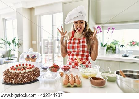 Beautiful young brunette pastry chef woman cooking pastries at the kitchen celebrating crazy and amazed for success with arms raised and open eyes screaming excited. winner concept 