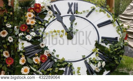 Large Wall Clock On The Field In Blooming Flowers, Showing The Time 11:55, 12:00. Time Management Co