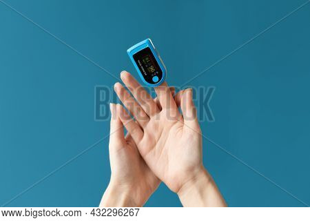Close Up Of Females Hand With A Pulse Oximeter Placed On The Index Finger. Blue Background. The Conc