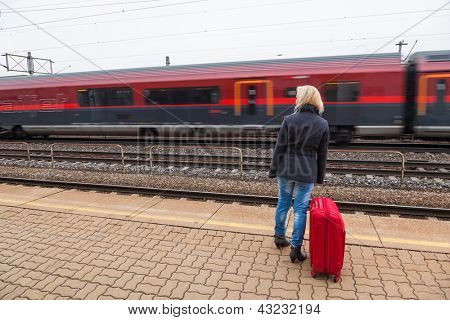 una giovane donna con i bagagli in attesa sulla piattaforma di una stazione per i treni. ritardo treno