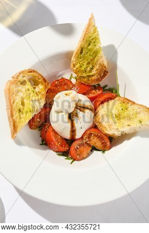Traditional Italian salad with Burrata cheese and tomatoes. Fancy caprese with burrata cheese, cherry tomatoes, pesto and balsamic sauces. Summer dish with mozzarella cheese on white table with shadow