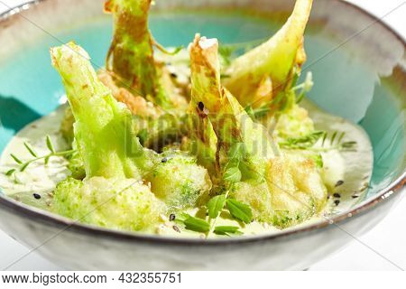 Fried tempura broccoli with peanut sauce in bowl. Vegeterian hot dish - florets cabbages roasted  in klar on white background. Veggie menu for asian restaurant. Hot vegan appetizers plant based