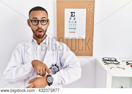 African american optician man standing by eyesight test in hurry pointing to watch time, impatience, upset and angry for deadline delay 