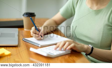 Young Female Taking Notes And Calculating With Calculator On Desk