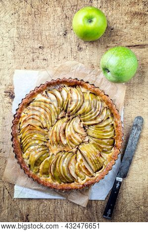 Traditional French apple cake offered as top view on a backing paper on a wooden board 