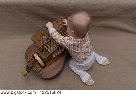 A Small Nine-month-old Child, Sitting On His Lap, Opens The Carved Cover Of The Keyboard Of An Ancie