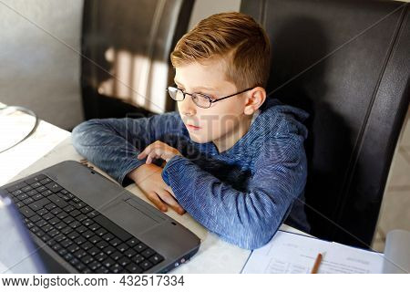 Happy Healthy Kid Boy With Glasses Making School Homework At Home With Notebook. Interested Child Wr