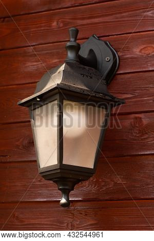Black Plastic Lantern With A White Light Bulb On A Wooden Wall