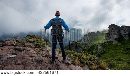 Rear View Of Hiker Standing On Top Of Rock On Mountain Peak