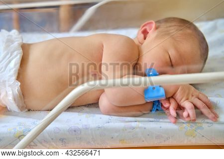 A Newborn Baby With A Maternity Hospital Bracelet On His Arm Is Sleeping In A Crib. A Newly Born Chi