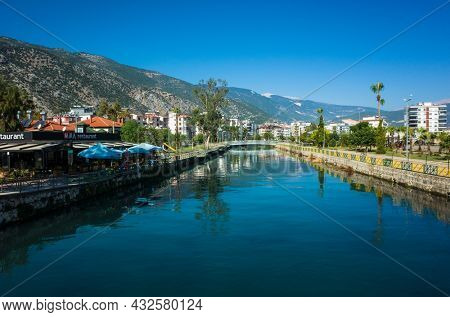 Finike, Turkey - 26 October, 2019: Akcay river with residential area and restaurant next to it, mountains on background, blue sky, province of Antalya