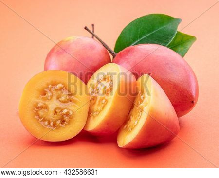 Ripe tamarillo fruits with slices and tamarillo leaves isolated on a orange background.