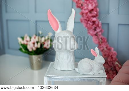 Two Ceramic Statuette Easter Bunnies Stand On A White Wooden Table. Easter Interior Home. Easter Hun