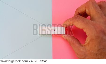 The Hand Shows The Hcg Test On A Blue And Pink Background And Shows Two Red Lines. A Pregnancy Test.