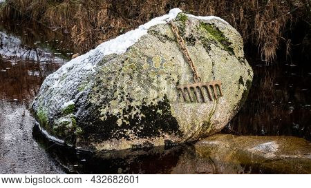 A Bronze Rake Attached To A Large Boulder By A Chain, Covered In Snow In Winter, On The Big Water Of