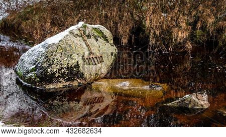 A Bronze Rake Attached To A Large Boulder By A Chain, Covered In Snow In Winter, On The Big Water Of