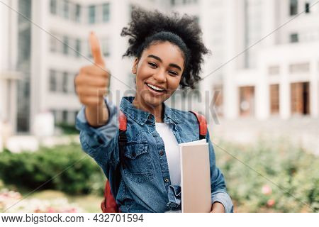Happy Black Female Student Gesturing Thumbs-up Holding Books Posing Outside