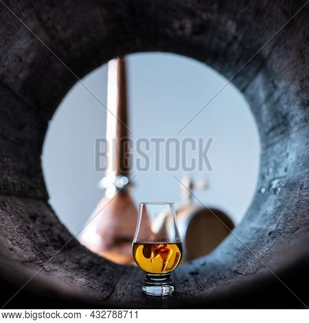 A glass of whiskey in old oak barrel. Copper alambic on background. Traditional alcohol distillery concept