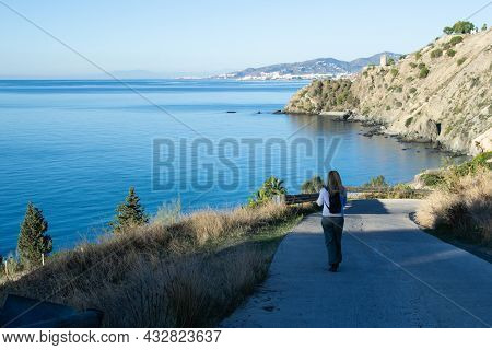 Woman With Blonde Hair Going Down A Small Road To The Beach Of Cañuelo Of Nerja With A Watchtower An