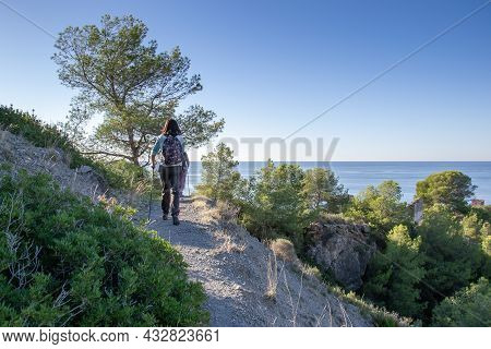Hiker Walking Along Narrow Path That Is In A Forest By The Sea On The Cliffs Of Maro Cerro Gordo