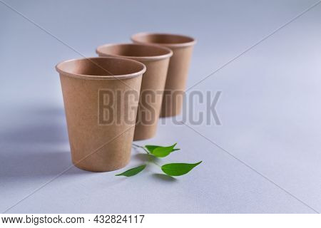 Three Paper Cups Stand With A Green Twig On A Gray Background. Eco Fendley Concept. Selective Focus.