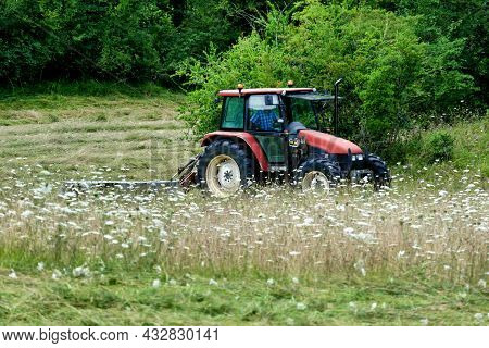 Tractor Cutting Grass In A Field Prior To Drying And Baling