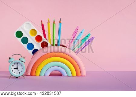 Pencil Case In The Form Of A Bright Rainbow With Paints, Pencils And A Ruler And An Alarm Clock On A