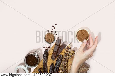 Organic Carob Pods, Powder, Chocolate And Carob Molasses On A Wooden Board In A Woman Hand On A Pink