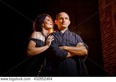 A Couple In Old Dark Clothes In An Abandoned Castle With Old Brick Walls. A Man And A Woman Posing I
